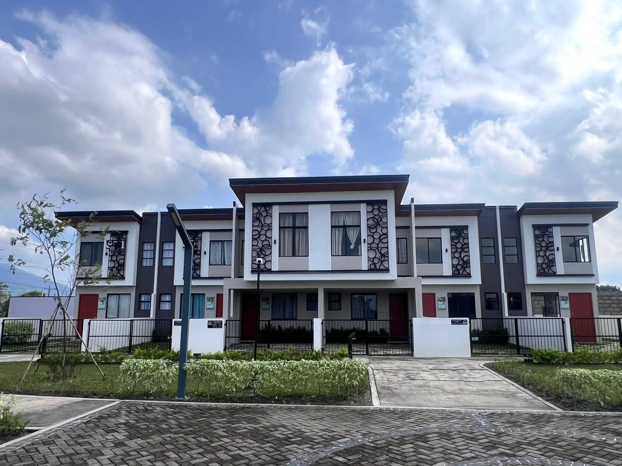 Modern two-story townhouses with decorative window screens under a bright, blue cloudy sky.